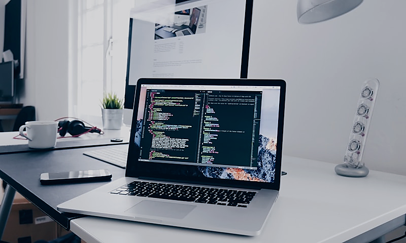 Web developer at a desk with laptop open to site layout and code, representing web design and development.